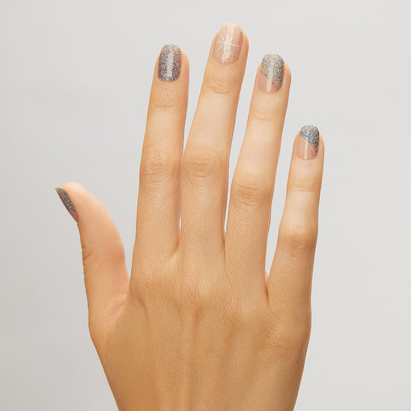Sheer nude gel nail strips featuring asymmetrical silver & blue glittered french tips, iridescent glitter, and snowflake accents with a double gel formula for an ultra-smooth finish.