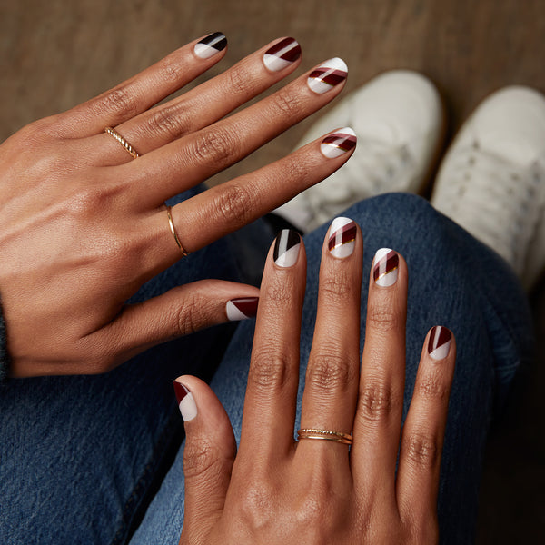 Sheer nude nail strips featuring maroon, chocolate, and white asymmetrical french tips and gold foil detail with a glossy, high-shine finish.