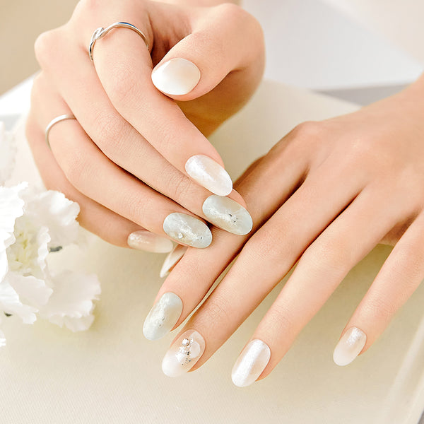 Long length, oval shape, glossy finish. Sheer white & soft green press-on gel nails featuring gold & silver glitter, rhinestones, and silver foil accents.